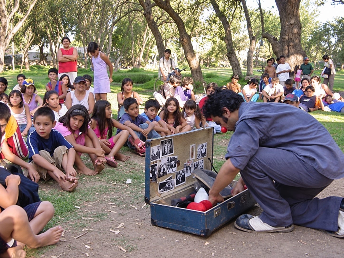 Niñas, niños y familias observan una función de Arte, circo y solidaridad en un parque