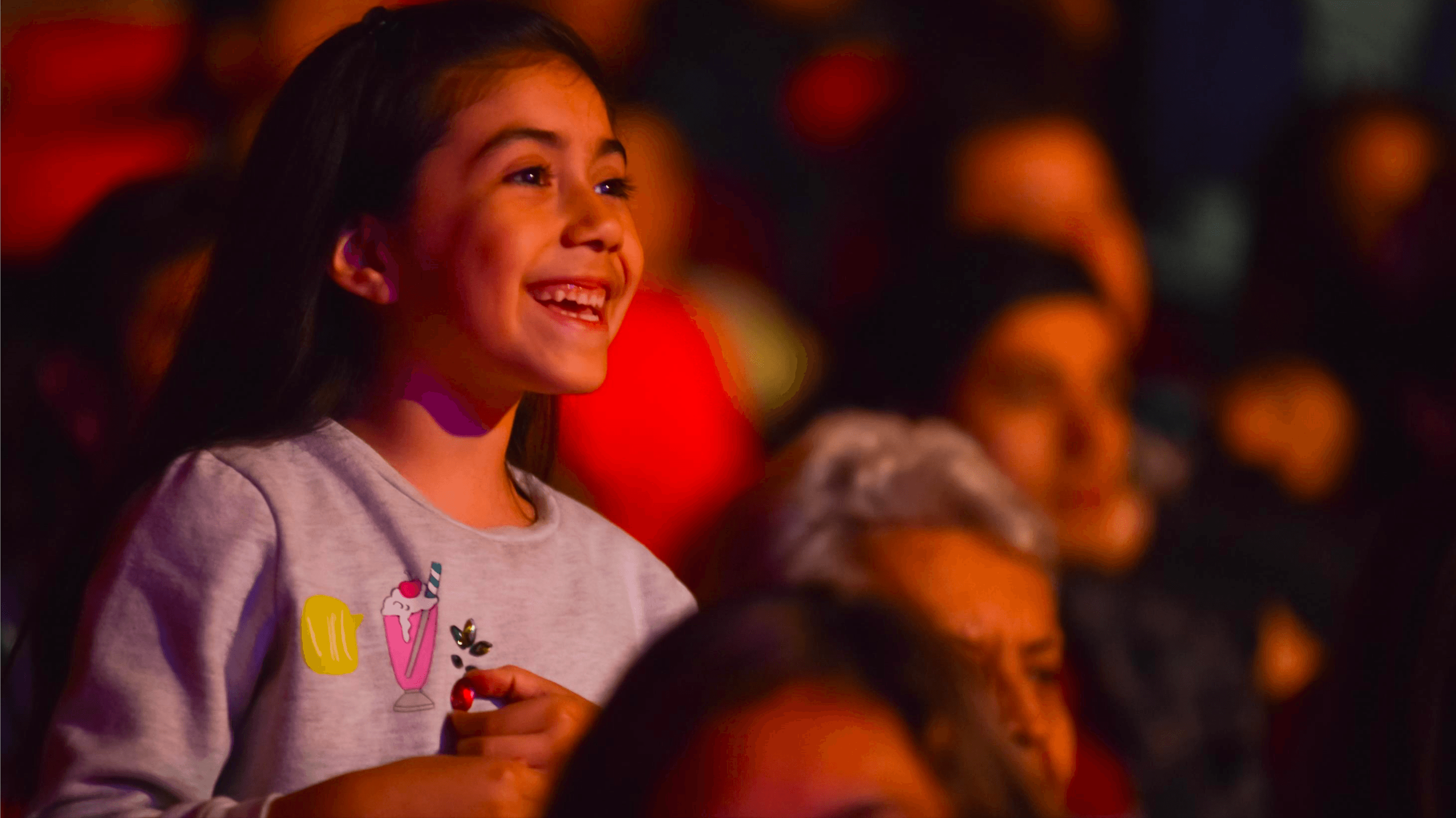 Niña sonríe entre el público durante una función de Atacamagica Kusiy