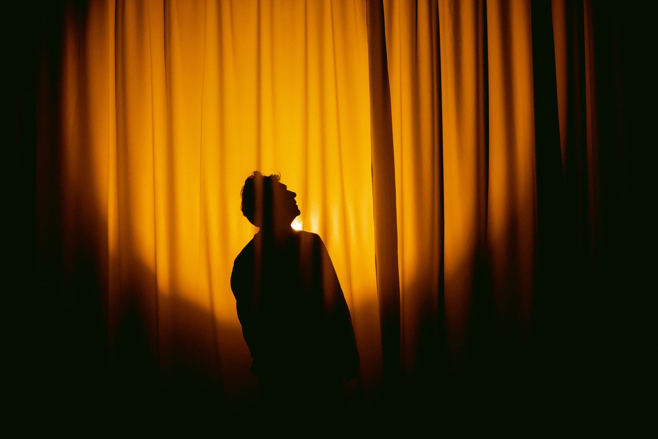 Silhouette of Luis Albornoz before an amber-lit curtain during Un mago en el desierto
